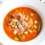 Minestrone soup sprinkled with Parmesan cheese in a white bowl
