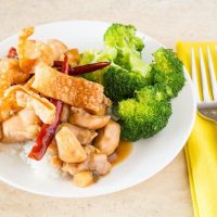 Sauteed General's Chicken with fried noodles and steamed broccoli on whit plate