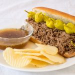 Italian Beef Sandwich with chips and au jus on a white plate