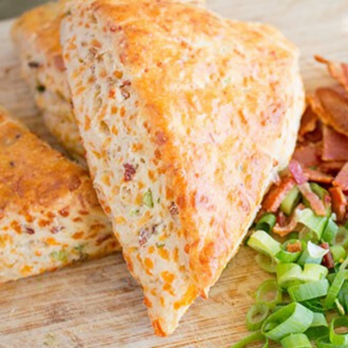 Scones on a wooden board with chopped bacon and green onions