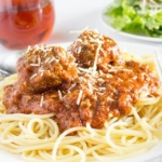 Spaghetti and meatballs on white plate with salad and a glass of wine