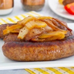 Bratwurst links topped with caramelized onions on a plate