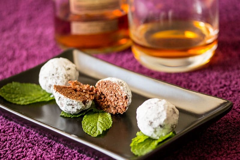 Chocolate Bacon Bourbon Balls in black plate and a glass of bourbon