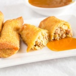 Egg roll cut in half with whole eggrolls and sweet and sour sauce on a plate