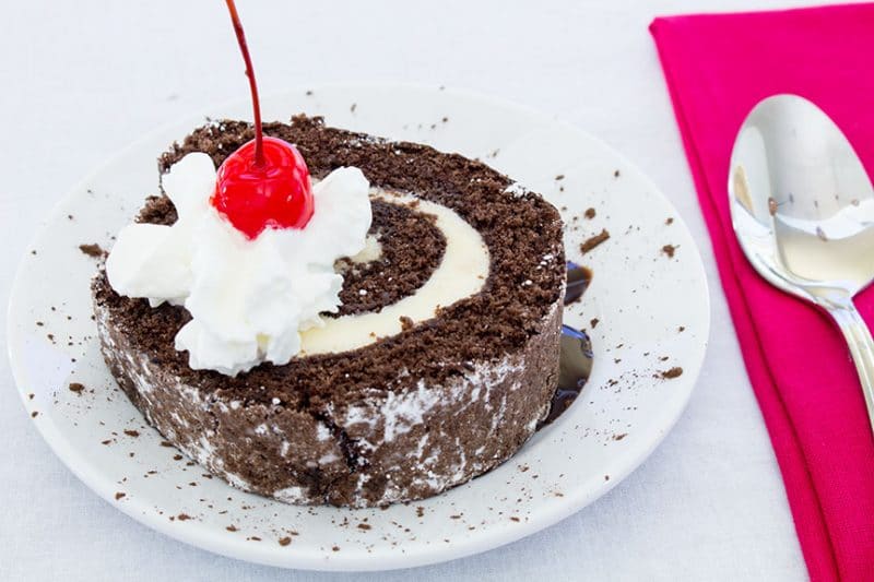 Ice Cream Cake roll with whipped cream and a cherry on white plate