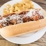 Meatball Sub with Shredded Parmesan Cheese and chips on white plate