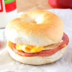 Bagel filled with Canadian bacon, fried egg, and cheese on a crinkled wrapper