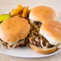Flat slider burgers with onions on white plate with pickles and french fries