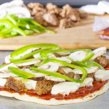 flatbread pizza with sauce, sausage, mozzarella cheese, mushrooms, and green peppers on a baking sheet