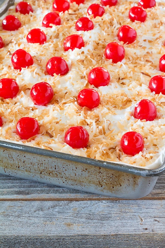 Cream of Coconut Cake - Rich coconut flavored cake soaked in sweetened condensed milk and cream of coconut, topped with toasted coconut and cherries. #recipe #dessert #cake #coconut