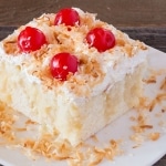 Close-up Cream of Coconut Cake with cherries and toasted coconut on white plate