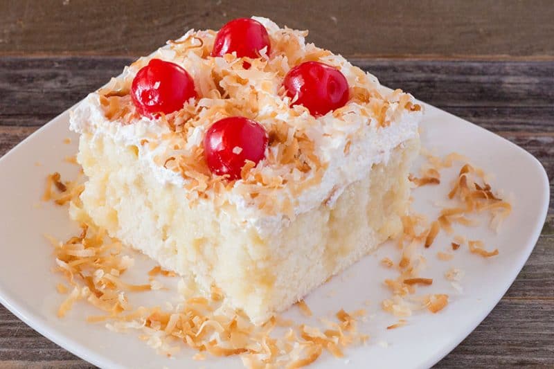 Close-up Cream of Coconut Cake with cherries and toasted coconut on white plate