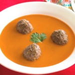 Tomato soup with thee meatballs and a parsley leaf