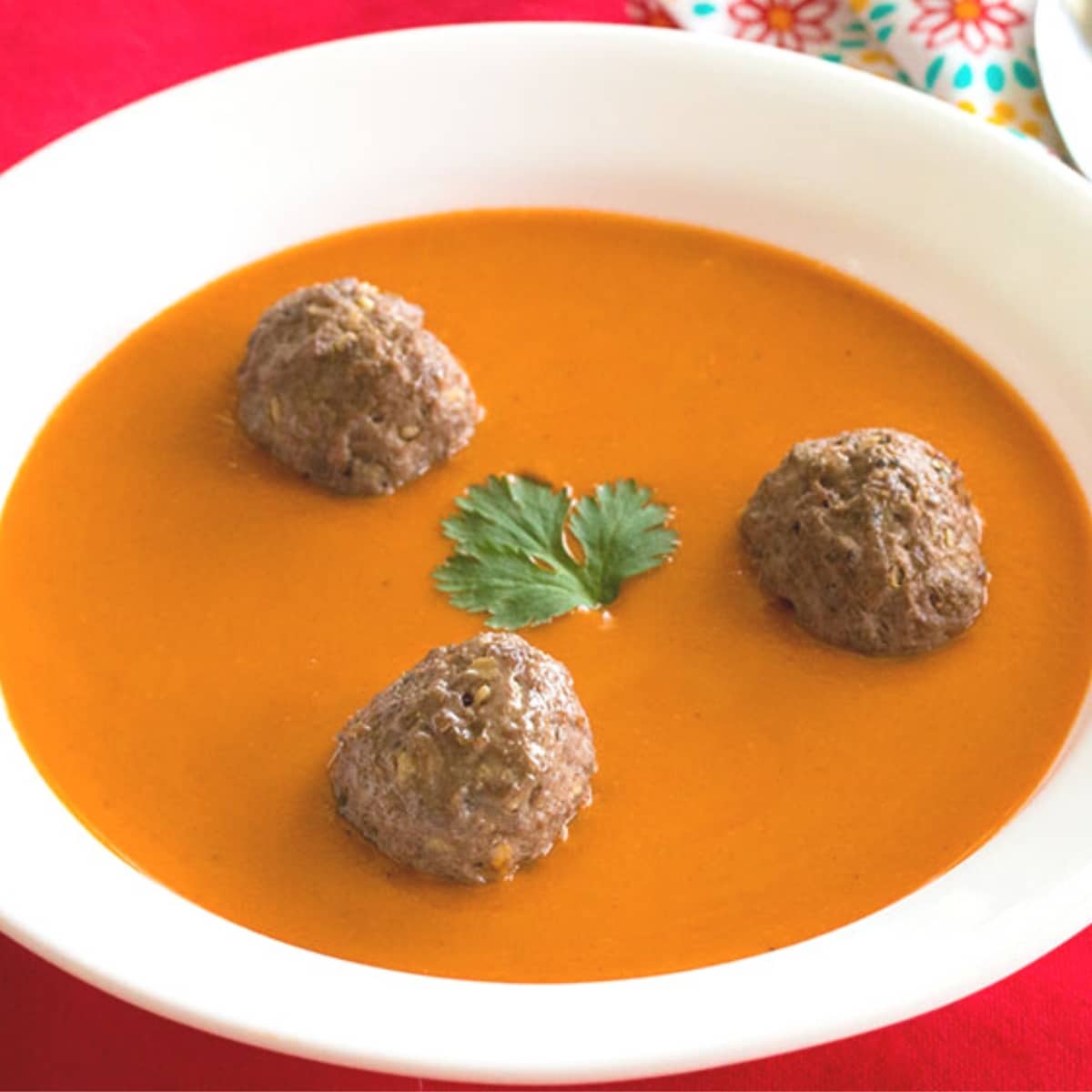 Tomato soup with thee meatballs and a parsley leaf