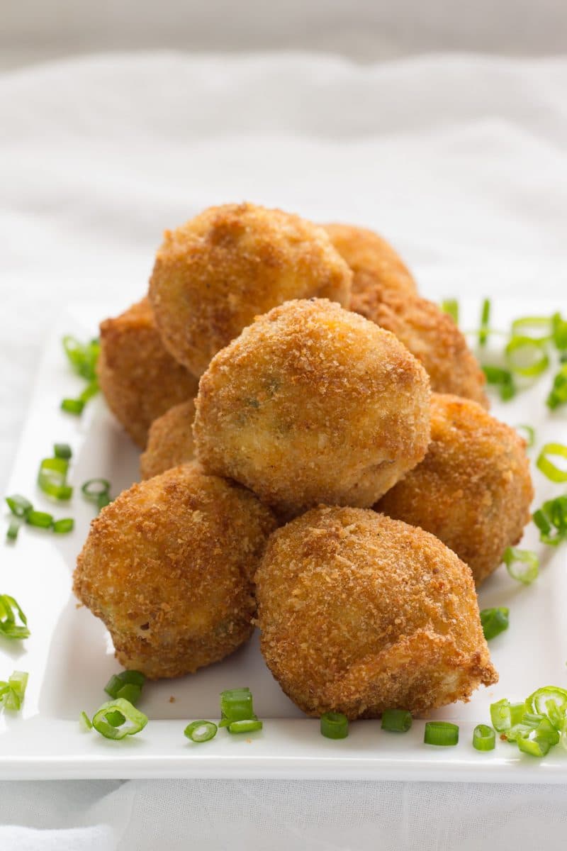 Fried potato balls on a plate with green onion pieces