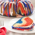 Slice of red white and blue pound cake on white plate with cut cake in background