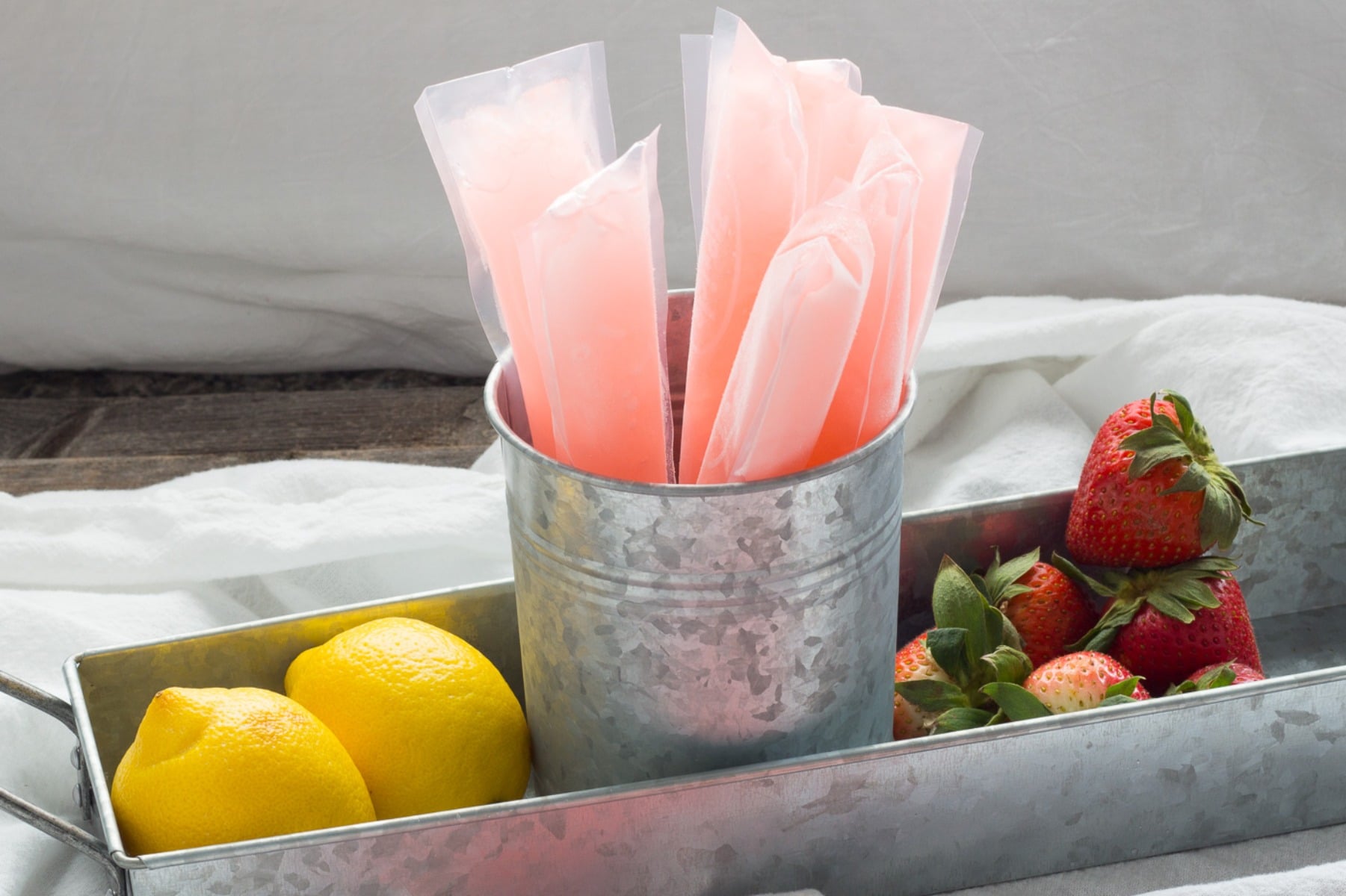 pink ice pops in a metal pail with whole lemons and strawberries