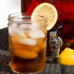 Sun tea in a glass with ice and a lemon wedge on the rim in front of a jar of tea