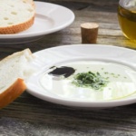 Fresh herb Italian Bread Dipping sauce on white plate with extra olive oil and balsamic vinegar and a plate of sliced bread
