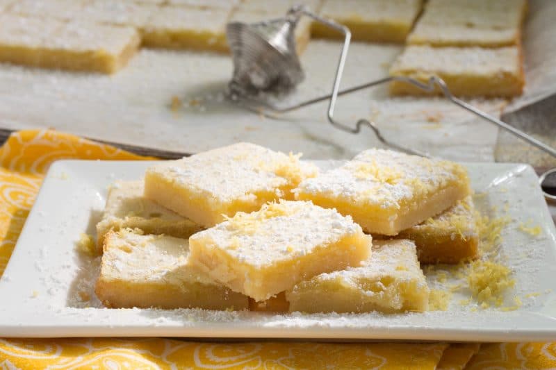 lemon bars on white plate with flour sifter in background