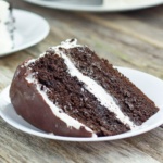 Slice of layered Chocolate cake with white frosting and a chocolate ganache topping