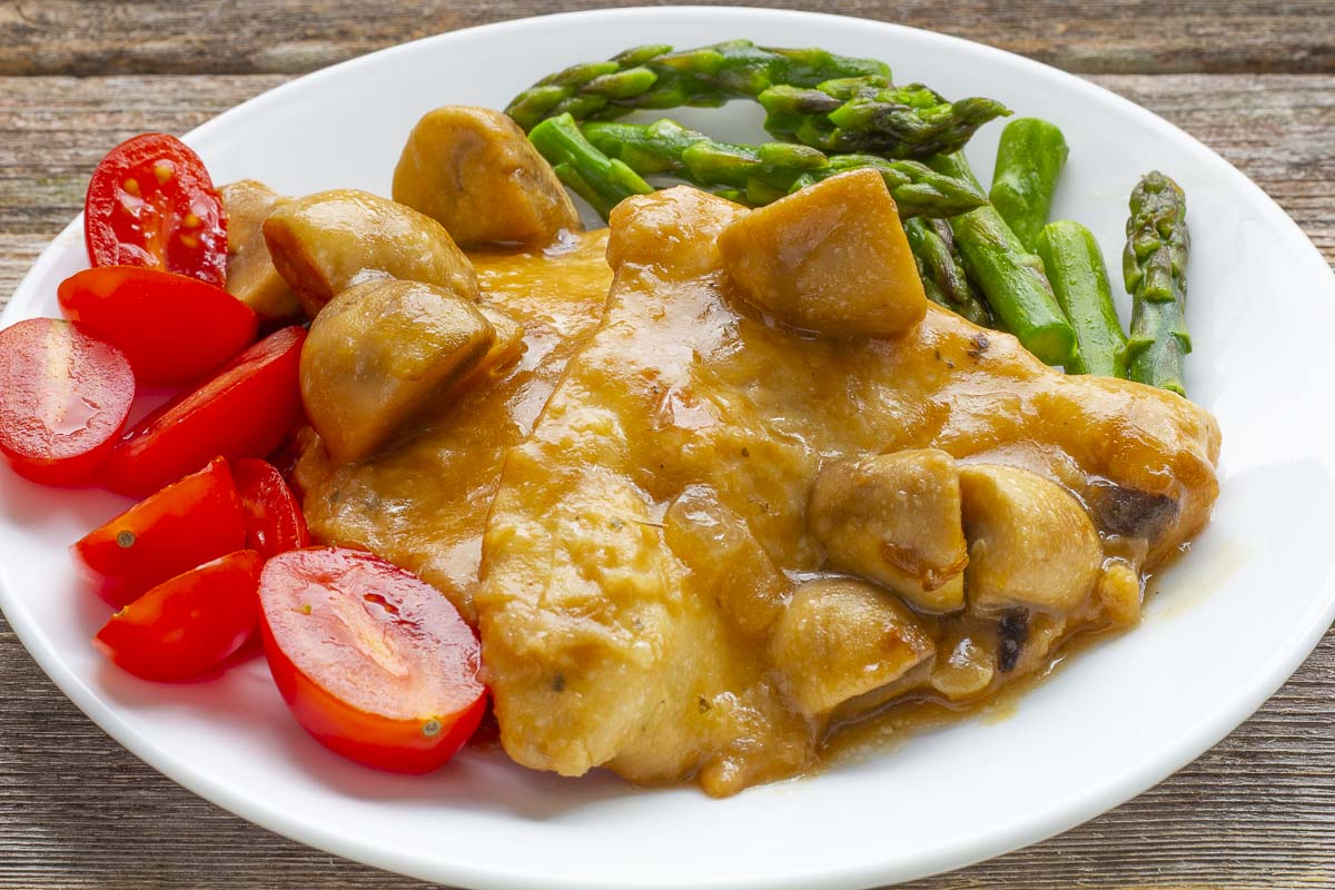 Chicken Marsala with asparagus and tomatoes on a white plate