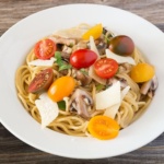 Spaghetti topped with tomatoes, mushrooms, and cheese