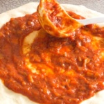 Pizza sauce with a spoon on a crust