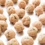 Formed uncooked turkey meatballs on a foil lined baking sheet