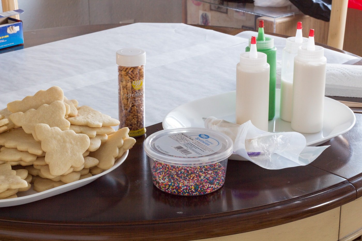 Cookie decorating station with cookies, icing in bottle, sprinkles and table covered in wax paper