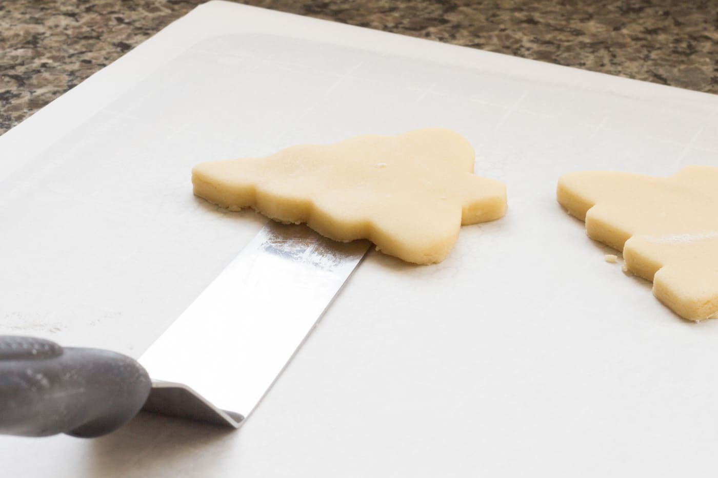 Cut out sugar cookie dough being transferred with an offset spatula onto parchment paper