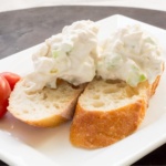 Scoops of chicken salad on sliced crusty bread on a plate
