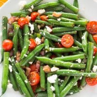 Fresh green bean salad in a white bowl sitting on a yellow cloth with white designs