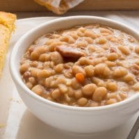 Southern ham and beans in a white bowl with a spoon and piece of cornbread