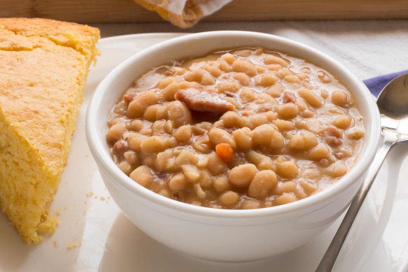 Southern ham and beans in a white bowl with a spoon and piece of cornbread