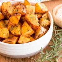 Paprika oven roasted potatoes in a white bowl with sour cream dipping sauce and rosemary sprigs