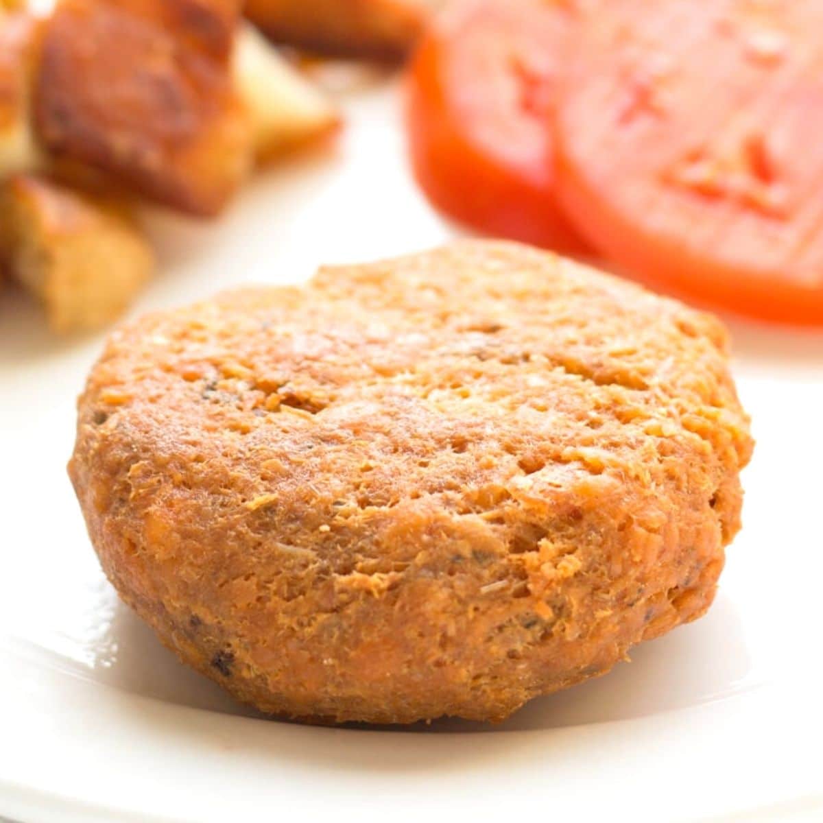 Salmon Patty on a plate with fried potatoes and tomato slices