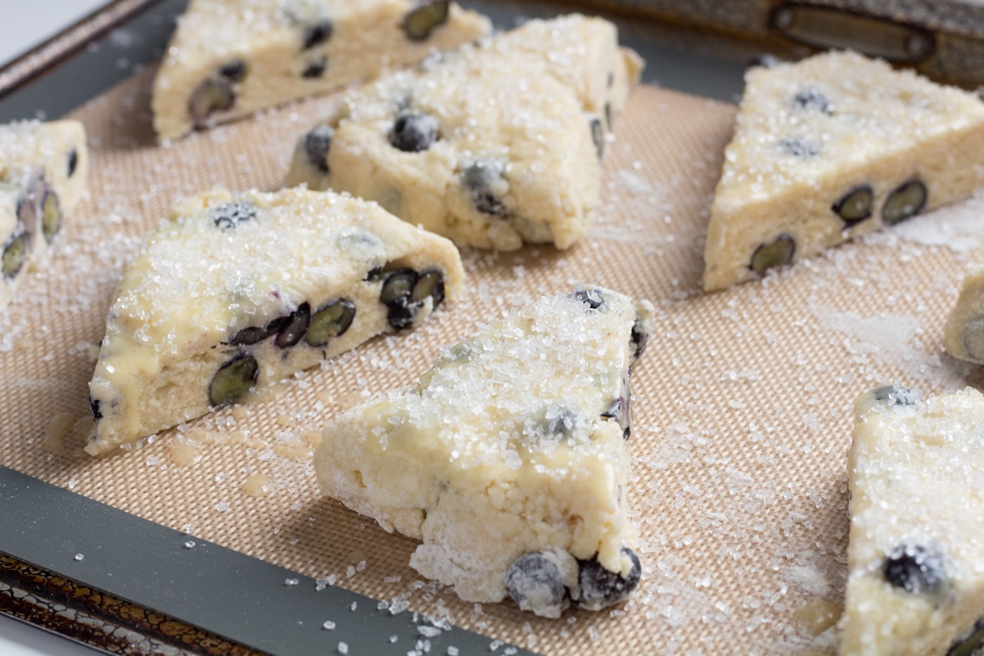 Cut blueberry scones topped with decorators sugar on a silicone baking mat