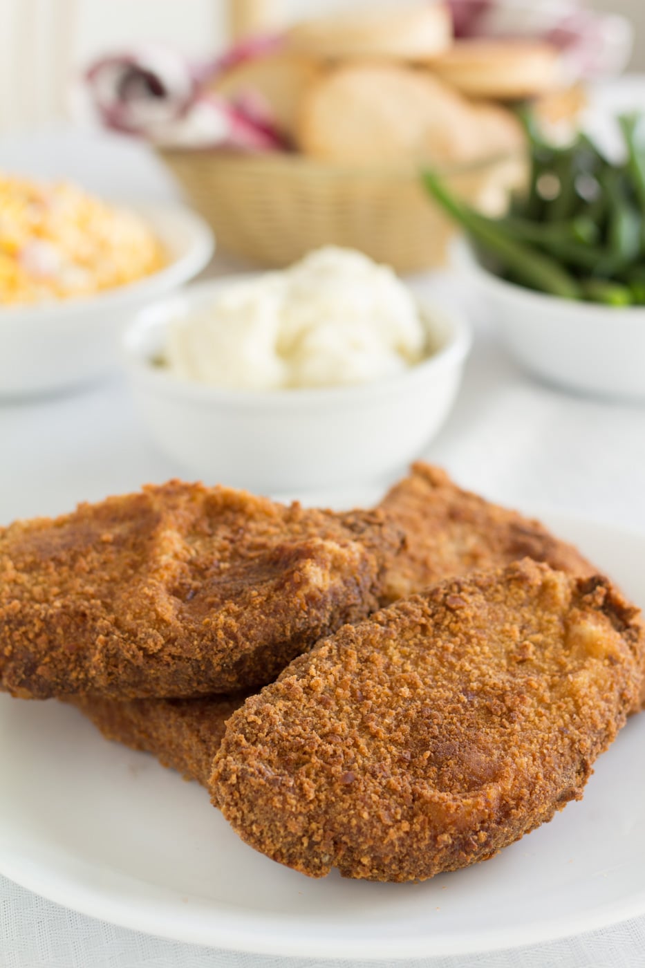 pork chops stacked on a white plate with side dishes in the background