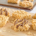 Peanut butter rice krispies treats with chocolate drizzle on a wooden board