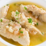 cooked chicken tenders with parsley flakes and a wine broth in a white bowl