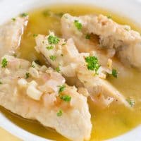 cooked chicken tenders with parsley flakes and a wine broth in a white bowl