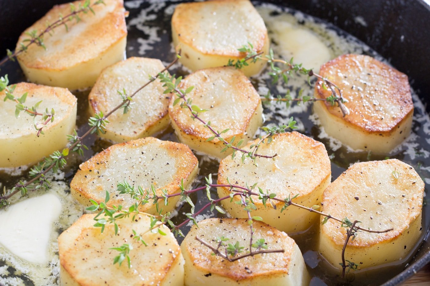 Browned potatoes with thyme sprigs in a skillet with oil and melting butter