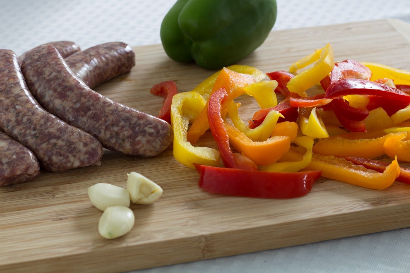 Italian sausage, bells peppers, and garlic on a wod cutting board