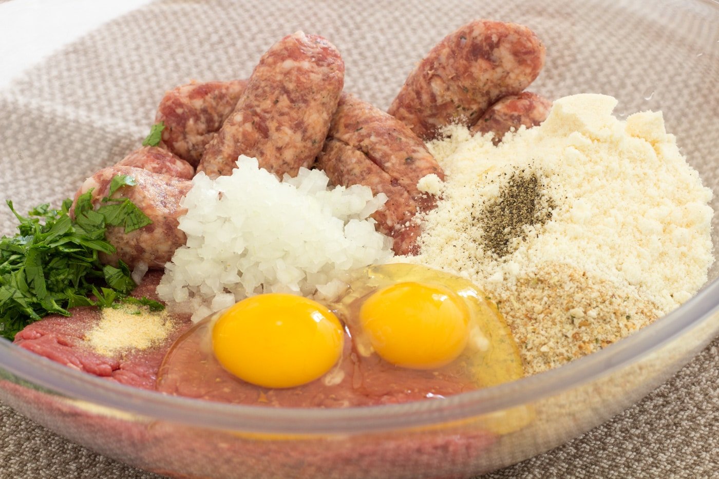 Italian sausage hamburger parmesan cheese eggs onions and parsley in a clear bowl