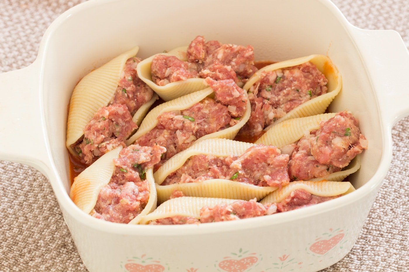 Raw meat filling packed in al dente jumbo pasta shells in a baking dish