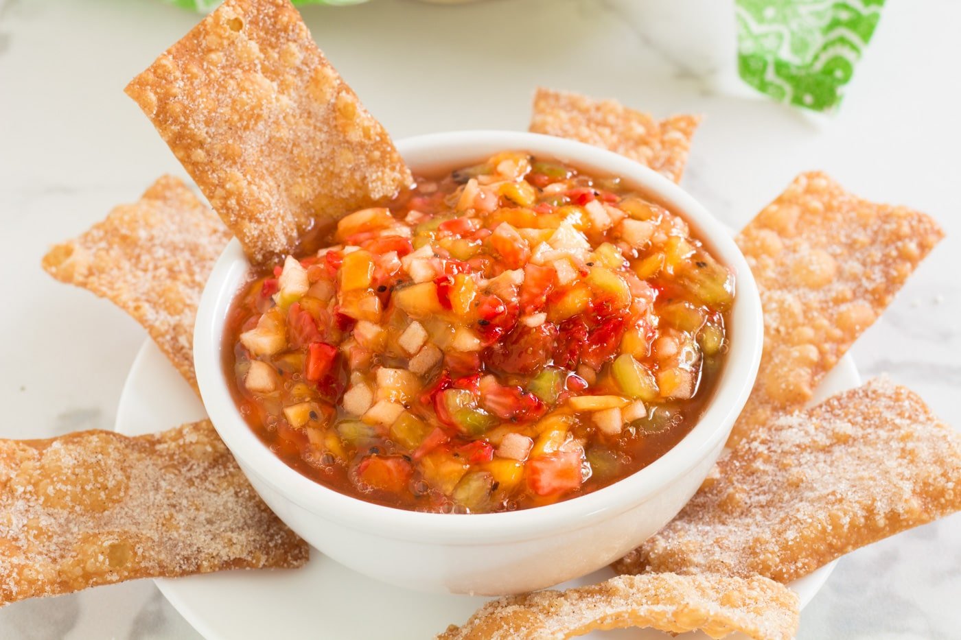 fruit salsa and cinnamon chip in a white bowl surrounded by cinnamon chips