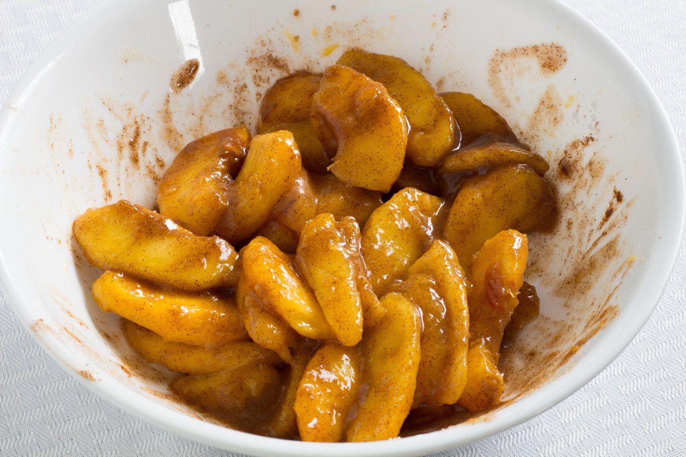 peaches coated in sugar and cinnamon in a white bowl