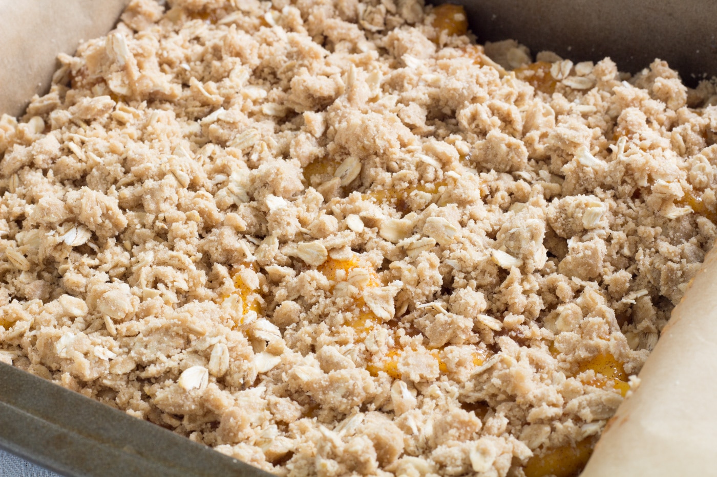 Brown sugar oat walnut topping sprinkled over peaches in a pan