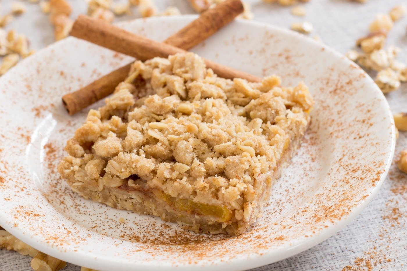 Oat based crust filled with peaches on a cinnamon sprinkled plate with cinnamon sticks